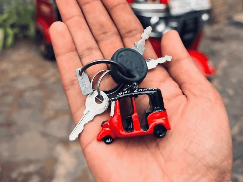 A hand holding tuk tuk keys with a red Sri Lanka tuk-tuk keyring after drop-off
