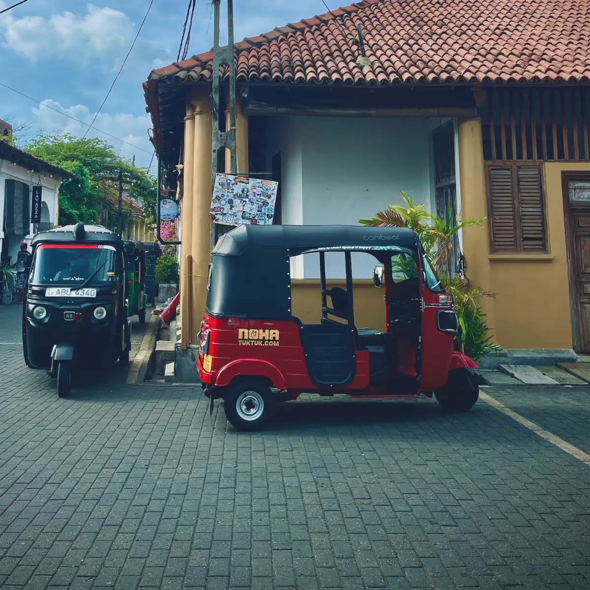 Side view of a red NOHA rental tuk tuk parked by Galle Fort's old walls