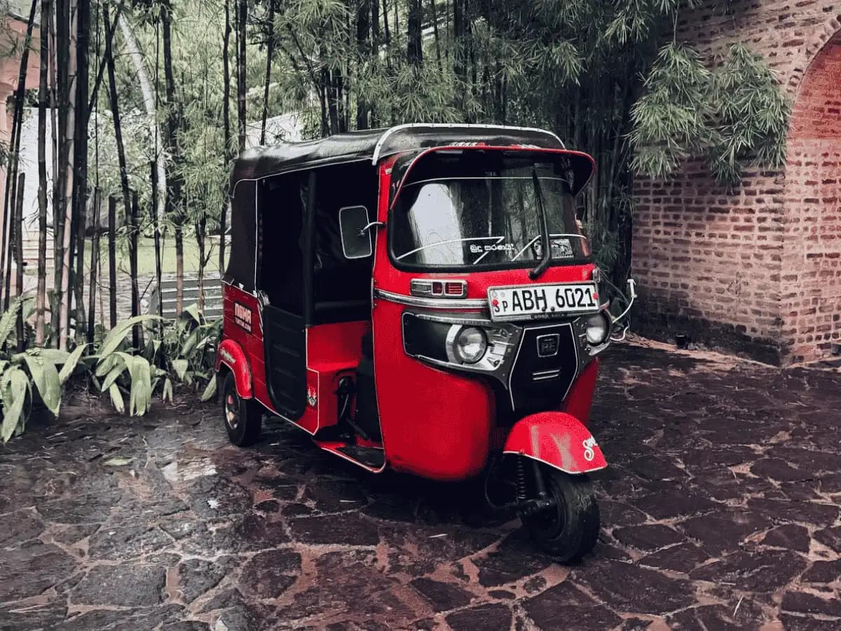 Red NOHA self-drive tuk tuk parked by a brick archway in Sri Lanka